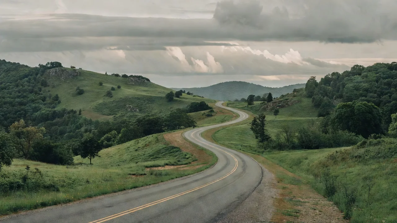 A two-lane road curving through green Appalachian foothills under a cloudy sky